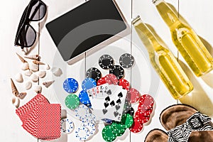 Card deck surrounded by poker chips and scattered seashells on white wooden background with copy space