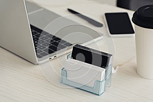 card holder with black and white empty business cards, laptop and smartphone with blank screen on office table.