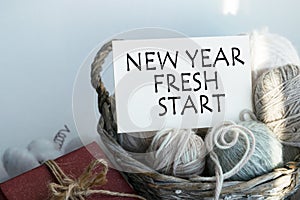 A card with the inscription NEW YEAR FRESH START in a basket with balls of thread. Delicate colors, light background.
