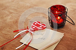 Card with Message With Love in the Letter, romantic candle holder with a candle and wooden red heart on a wooden table