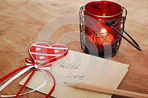 Card with Message With Love in the Letter, romantic candle holder with a candle and wooden red heart on a wooden table