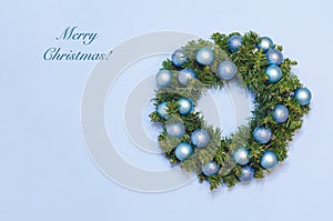 Card with modern Christmas winter wreath on the door of fir branches with balls on blue background on New Year`s Eve.