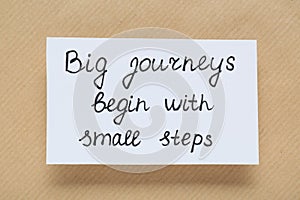 Card with phrase Big Journeys Begin With Small Steps on beige background, top view. Motivational quote