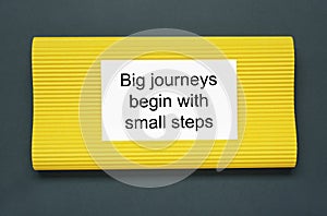 Card with phrase Big Journeys Begin With Small Steps on dark background, top view. Motivational quote