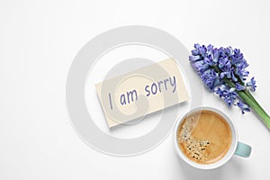 Card with phrase I Am Sorry, hyacinth flowers and cup of coffee on white background, flat lay. Space for text