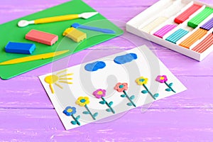 Card with plasticine flowers, sun and clouds. Plasticine set on a wooden table. Children modeling clay art. Crafts idea