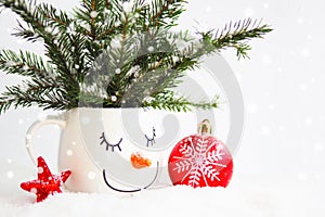 card snowy fir branches in a cup with the face of a sleeping snowman, a red Christmas ball and a star