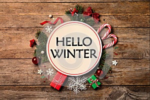 Card with text Hello Winter, gift boxes and Christmas decor on wooden background, flat lay