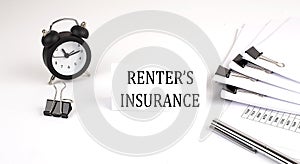 Card with text RENTER`S INSURANCE on a white background, near office supplies and alarm clock. Business concept