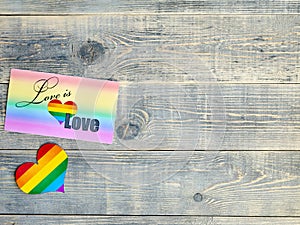 Card on which is written love is love with a rainbow background and a heart with the LGBT flag lie on a light blue textured wooden