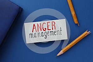 Card with words Anger Management, notebook and broken pencil on blue background, flat lay photo