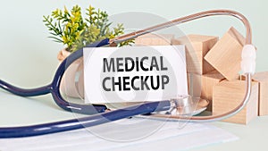 Card with words MEDICAL CHECKUP, stetoscop, wooden blocks and flower on table photo