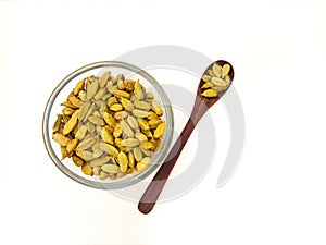 Cardamom pods in glass bowl with wooden spoon on white background, Top view