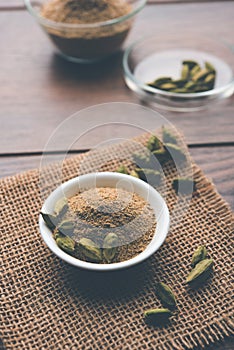 Cardamom powder or elaichi powder in bowl over moody background with pods.