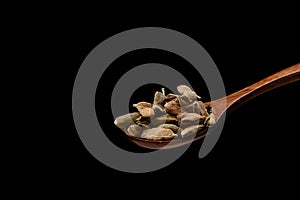 Cardamom seeds on wooden spoon over black background.