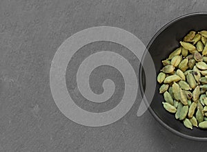 Cardamon seeds in bowl on grey table