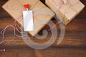 Cardboard box with clothpin with red heart and empty white label with place for text on a brown wooden background