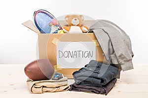 Cardboard box with donation clothes and different objects on white