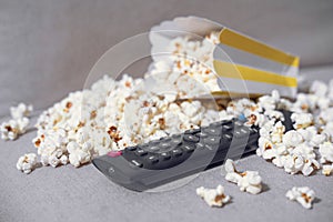 The cardboard box with popcorn and remote control on grey background. Concept of hobby or pleasant time spending at home, watching