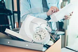 Cardboard box and resignation letter, dossier, alam clock, coffee cup, calculator and drawing tube in box. Quiting a job,