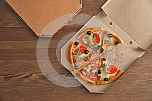 Cardboard box with tasty pizza on wooden background, top view.
