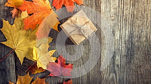 cardboard box tied with string on a bow on a wooden background in autumn leaves, holiday gift on Thanksgiving Hellouin. view from