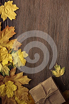 cardboard box tied with string on a bow on a wooden background in autumn leaves, holiday gift on Thanksgiving Hellouin. view from