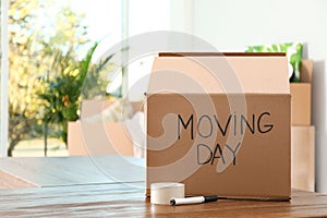 Cardboard box with words MOVING DAY and packaging items on table