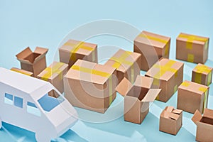 Cardboard boxes near van model on blue background with copy space.