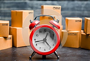 Cardboard boxes and red alarm clock. Time of delivery. Limited supply, shortage of goods in stock, hype and consumer fever. Time photo