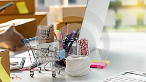 Cardboard boxes in a small shopping cart on the desk and laptop on the side with new thread. An online shopping idea where