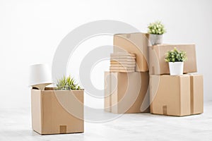 Cardboard boxes with things are stacked on the floor against the background of a white wall close up. Books and table