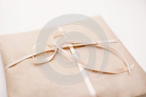 Cardboard carton package wrapped with light brown paper and tied with pink string ribbon in bow