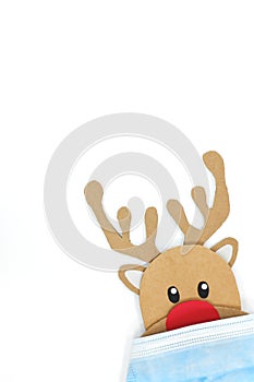 Cardboard cutout of Rudolph the red-nosed reindeer peeking while wearing a face mask. Covid during Christmas