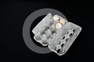 Cardboard egg box with three eggs on black mat background