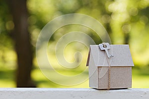 Cardboard house with key against green bokeh. Building, loan, housewarming, insurance, real estate or buying new home.