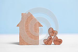 Cardboard house and wooden hearts with inscriptions Love on blue and white background