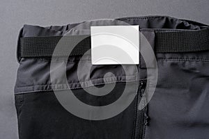 Cardboard label attached to the waistband of dark gray outdoor trousers