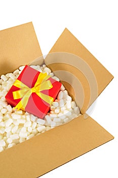 Cardboard shipping box, small red christmas gift inside, styrofoam polystyrene packing pieces
