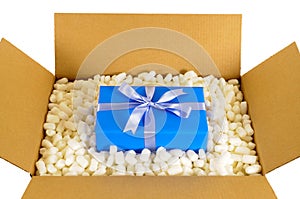 Cardboard shipping delivery box with blue gift inside and polystyrene packing pieces, top view