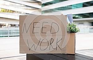 Cardboard sign with 'Need Work' text alongside personal items