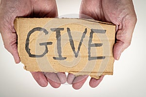 A cardboard sign in palm of hands with the word give. Generosity theme.