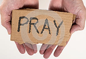 Cardboard sign with PRAY written on it held in palm of hands