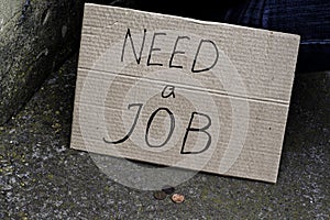 The cardboard tablet with the inscription need a job next to an unemployed person sitting on the ground are small coins