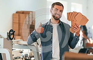 With cardboards. Handsome man is working at the factory of creating eco boxes