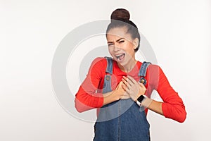 Cardiac problems. Portrait of young fatigued woman with hair bun in denim overalls clasping chest, feeling acute pain