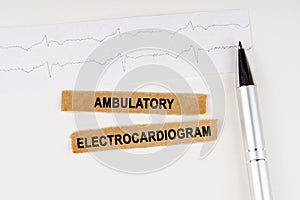 On the cardiogram lies a pen and torn paper with the text - Ambulatory Electrocardiogram