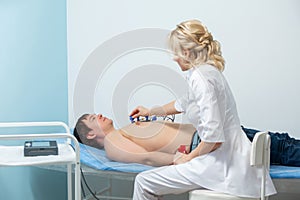 A cardiologist doctor applies sensors to the naked body of a man lying on a couch during an electrocardiography