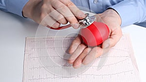 Cardiologist doctor checks heart rate on a toy red heart. Phonendoscope, stethoscope and cardiogram. Healthcare and early diagnosi
