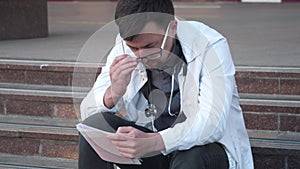 Cardiologist holding and review electrocardiograph EKG or ECG diagram sitting outside hospital on stairs. Young doctor